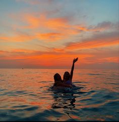 two people in the water at sunset, one raising her arm up to the sky