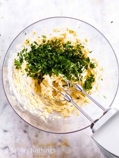 a glass bowl filled with mashed potatoes and parsley on top of a marble counter