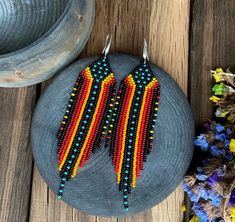 two pairs of beaded earrings sitting on top of a wooden table next to flowers