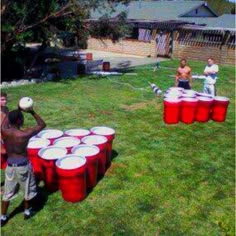 two people playing with red plastic buckets on the grass, and another person standing in front of them