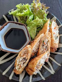 a black plate topped with food next to a bowl of sauce and lettuce