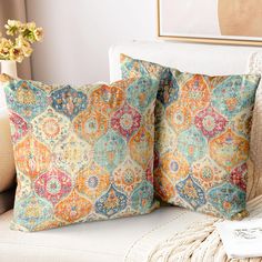 two decorative pillows sitting on top of a white couch next to a vase with flowers