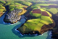 an aerial view of the coast with green fields and houses in the foreground, surrounded by blue water