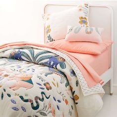 a white bed topped with pillows and blankets next to a pink comforter on top of a wooden headboard