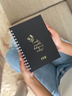 a woman is holding a notebook with writing on it and the cover has gold foil