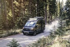 a black van driving down a dirt road in the woods with trees on both sides