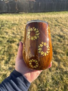 a hand holding a wooden wine glass with flowers painted on the outside, in front of a fence