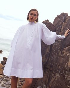 Our whimsical signature poplin shirt dress, crafted from soft Italian cotton, showcases pleating along the shoulders and back, creating a beautifully flowing silhouette. It features exaggerated bustled sleeves, worn multiple ways, crisp inverted buttoned cuffs, and inseam side pockets. Detailed with covered buttons and a versatile asymmetrical neckline, it strikes the perfect balance between masculine structure and feminine elegance, offering effortless sophistication, day or night. A must-have Poplin Shirt Dress, Feminine Elegance, Puff Sleeve Shirt, Asymmetrical Neckline, Dress Shirt Sleeves, Poplin Shirt, British Indian, Covered Buttons, Dress Accessories