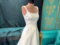 a mannequin wearing a white wedding dress in front of a blue chair and wall