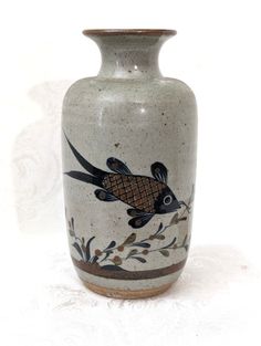 a white vase with a fish painted on it's side and leaves in the bottom