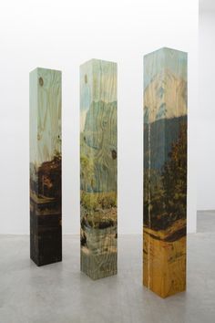 three tall wooden sculptures sitting on top of a cement floor