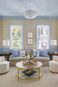 a living room with couches, chairs and tables in front of two large windows