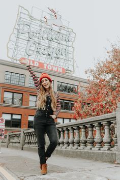 a woman standing on the sidewalk in front of a building with a neon sign above her head