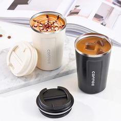 two coffee cups sitting next to each other on a marble counter top with a book and magazine in the background