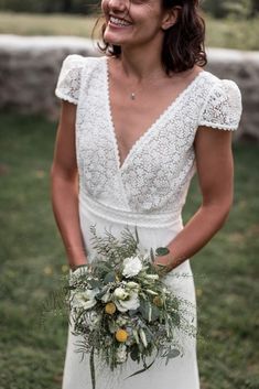 a woman in a white dress is holding a flower bouquet and smiling at the camera