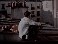 a man sitting on top of a roof next to a woman laying down in front of him