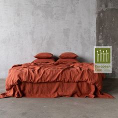 an orange bed with two pillows on it in front of a concrete wall and cement floor