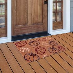 a door mat with pumpkins on it sitting in front of a wooden entryway