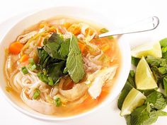 a bowl of chicken noodle soup next to sliced limes and cilantro