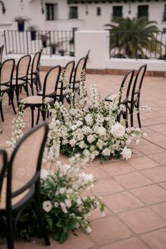 rows of black chairs with white flowers on the floor in front of an outdoor venue