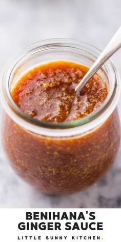 a jar filled with barbecue sauce on top of a white counter next to a wooden spoon