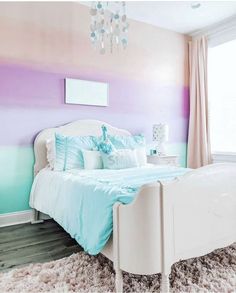 a white bed sitting under a chandelier in a bedroom next to a window