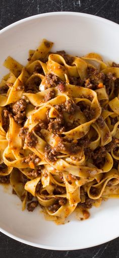 a white bowl filled with pasta and meat sauce on top of a black countertop