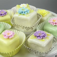 there are many small cakes with flowers on the top one is white and has yellow frosting