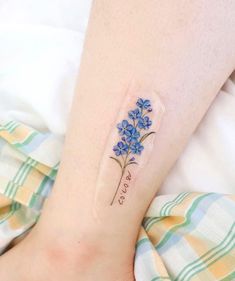 a small blue flower tattoo on the left side of the leg, with words written below it