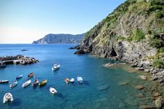 several boats are anchored in the clear blue water near a rocky cliff and shore line