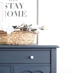 a basket with flowers sitting on top of a blue dresser next to a sign that says stay home