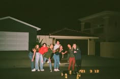 a group of people standing around each other in front of a house at night time