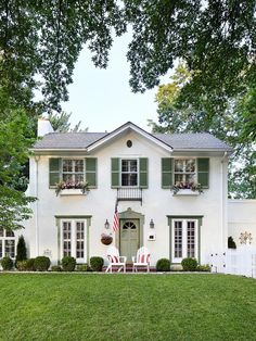 a white house with green shutters and two lawn chairs