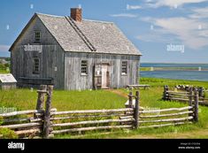 an old wooden house sitting on top of a lush green field next to the ocean