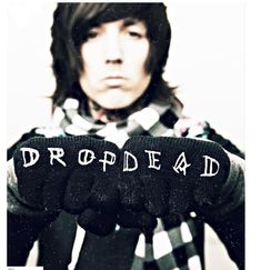 a man with long hair and black gloves holding up the word drop dead on his hands