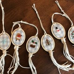 four cross stitch christmas ornaments hanging from string on a wooden table with tassels