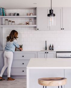 a woman standing in a kitchen next to a counter top and cabinets with white cupboards