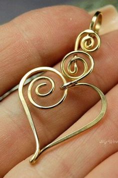 a hand holding a gold pendant with two spirals on the front and one in the back