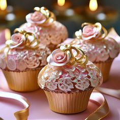 three cupcakes decorated with pink and gold icing on a pink plate next to candles