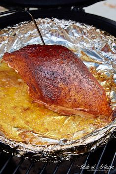 a piece of meat is on top of tin foil over an open fire pit with tongs