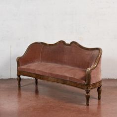 an old fashioned wooden couch sitting on top of a hard wood floor next to a white wall