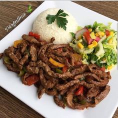 a white plate topped with meat and veggies next to rice on top of a wooden table