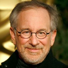 an older man wearing glasses and a black turtle - neck sweater smiles at the camera