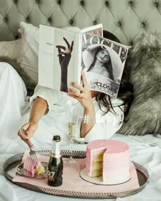 a woman reading a magazine while laying in bed with a slice of cake on the tray