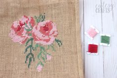 a piece of burlock with some pink flowers on it next to two spools of thread