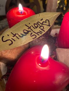 two red candles sitting next to each other on top of a wooden table with writing on them