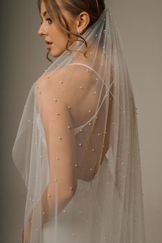 a woman wearing a wedding veil with pearls on the back of her head and shoulders