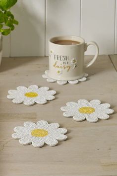 three white and yellow daisy coasters next to a cup of coffee on a table