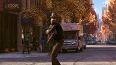 a man is playing guitar on the street in front of some buildings and trees with fall colors