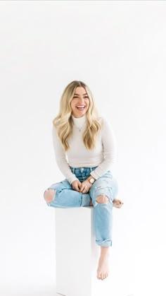 a woman sitting on top of a white box with her legs crossed and wearing ripped jeans